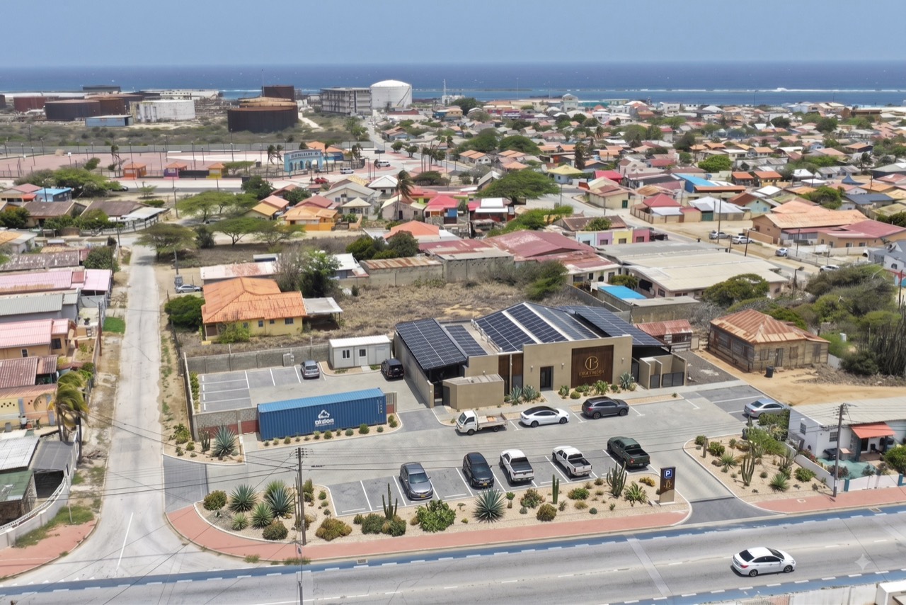 Aerial view of a completed Casabella building in Aruba — a single-storey block with private backyards, a pool terrace and a solar array on the roof.